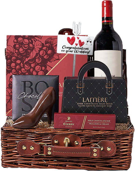 A wicker basket containing a bottle of red wine, chocolate items including a shoe-shaped piece, and a card with "Congratulations on your Wedding!" text and heart illustrations.