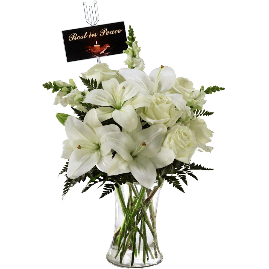 A glass vase with a bouquet of white lilies and roses, accented by green foliage. A card with the message "Rest in Peace" is attached to the arrangement.