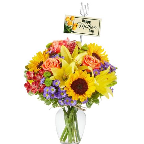 A vibrant bouquet featuring sunflowers, yellow lilies, orange roses, red and green chrysanthemums, and purple daisies in a clear vase, adorned with a "Happy Mother's Day" card.