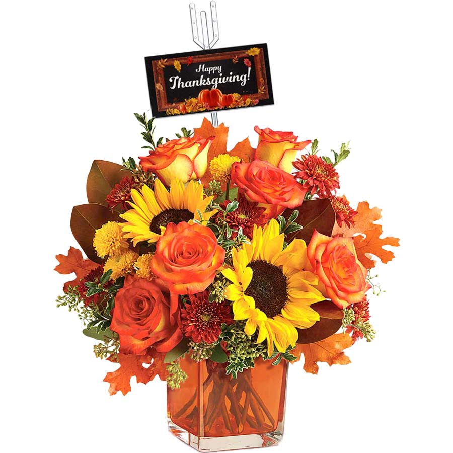 A vibrant Thanksgiving bouquet with sunflowers, orange roses, and autumn leaves in a square glass vase. A decorative card with "Happy Thanksgiving!" is attached to the arrangement.